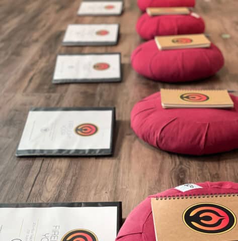 Teacher training manuals and notebooks lined up on the floor for trainees, with red meditation cushions.