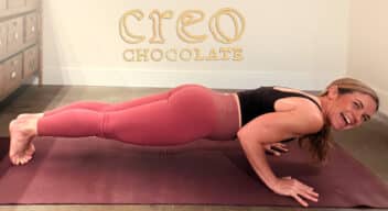 Woman smiling in a Chaturanga Yoga pose with the Creo Chocolate logo on the wall above her.