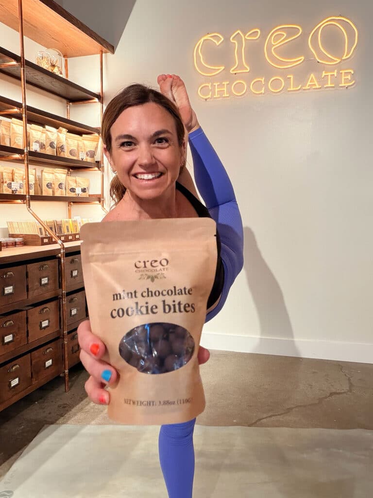 Jamie in standing bow pose, holding a bag of Creo's mint chocolate cookie bites.