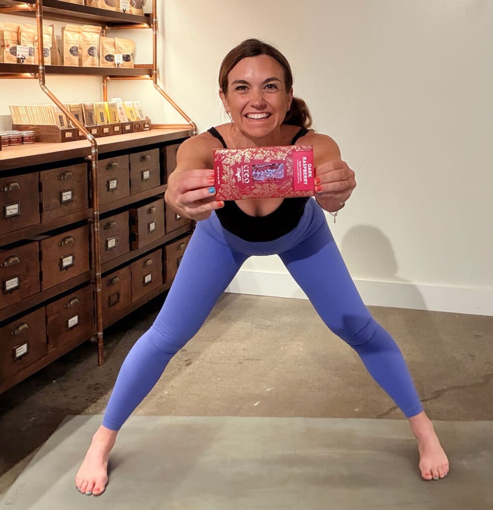 Jamie in a wide-leg forward fold, holding a Creo Chocolate Bar