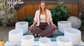 Woman sitting on blanket outside surrounded by crystal singing bowls.