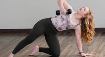 Woman in a modified side plank with a hand weight in the upper arm doing rows.