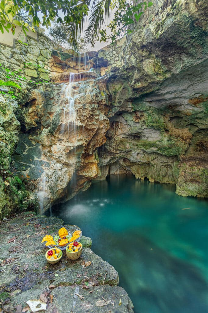 Freshwater cenote with colorful bowls of fruit on the rocks.